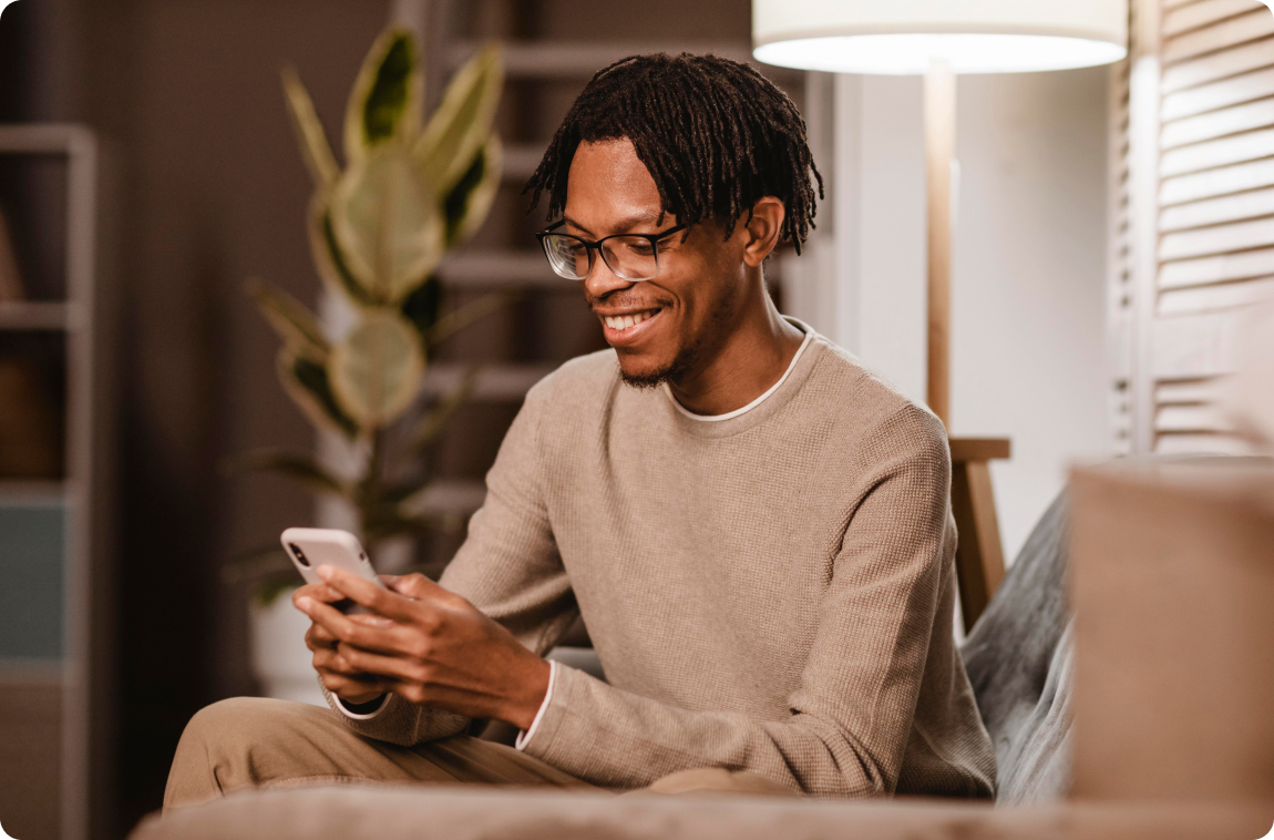 homem negro com moletom bege mexendo-no celular e sorrindo